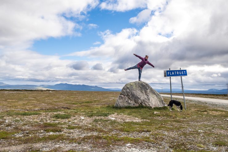 Kvinna står på stor sten bredvid vägskylt för Flatruet