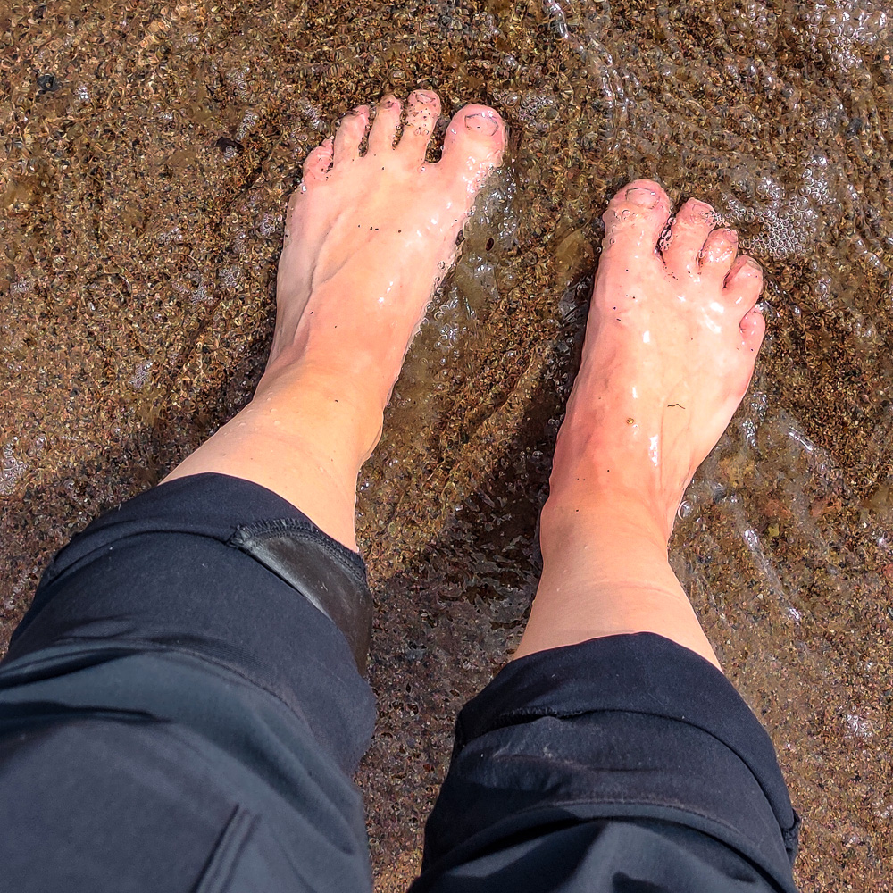 Svalkar fötter i vattnet i strandkanten