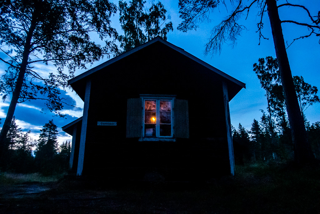 Ljus brinner i köket i Prästvallsstugan, sett utifrån i skyminingen