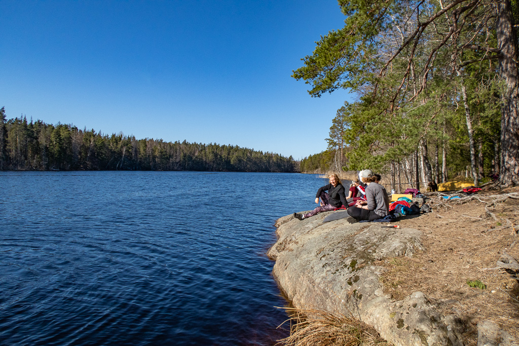 Människor sitter på klippa vid sjö i solen