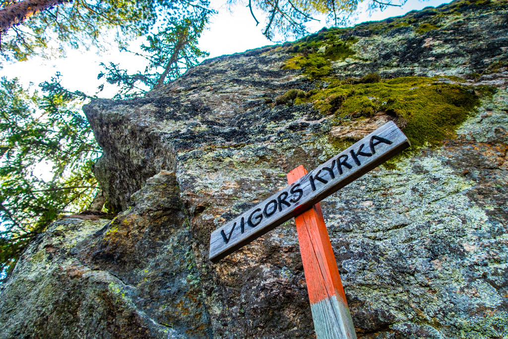 Skylt med texten Vigors kyrka, framför stor sten 