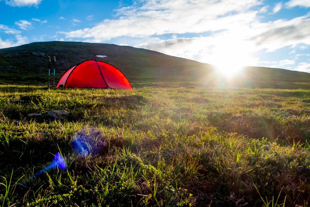 Solen skymtar bakom fjäll med tält i förgrunden